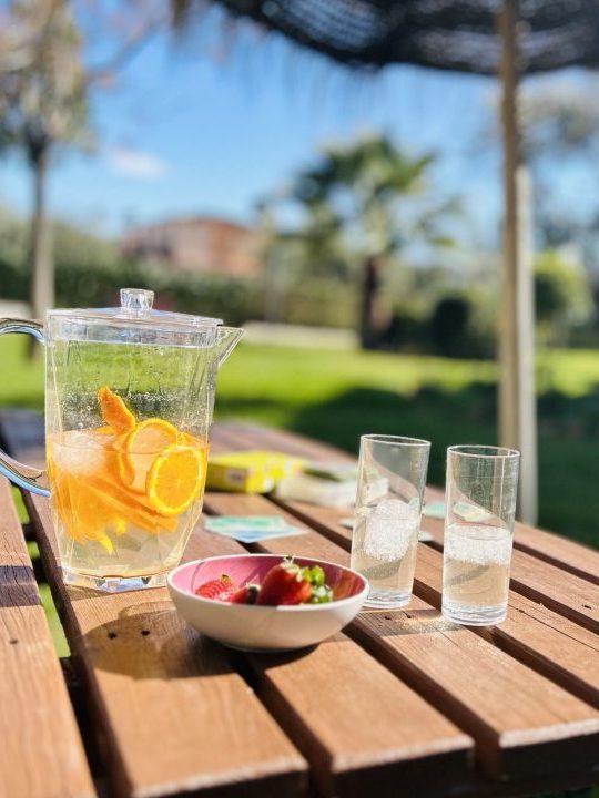 Naranjada, vasos y bol de fresas sobre mesa de camping de madera